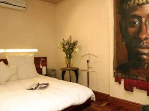 White bed and fresh flowers beside a painted African portrait in the Luxury Room at Rosedene Lodge